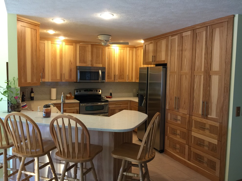Photo of a small traditional u-shaped kitchen/diner in Omaha with a submerged sink, shaker cabinets, medium wood cabinets, engineered stone countertops, white splashback, stainless steel appliances, porcelain flooring, a breakfast bar, beige floors and white worktops.
