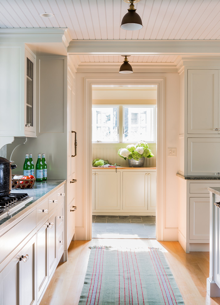 Klassische Wohnküche mit Unterbauwaschbecken, Kassettenfronten, weißen Schränken, Granit-Arbeitsplatte, Küchenrückwand in Grün, Rückwand aus Glasfliesen, Küchengeräten aus Edelstahl, hellem Holzboden und Kücheninsel in Boston