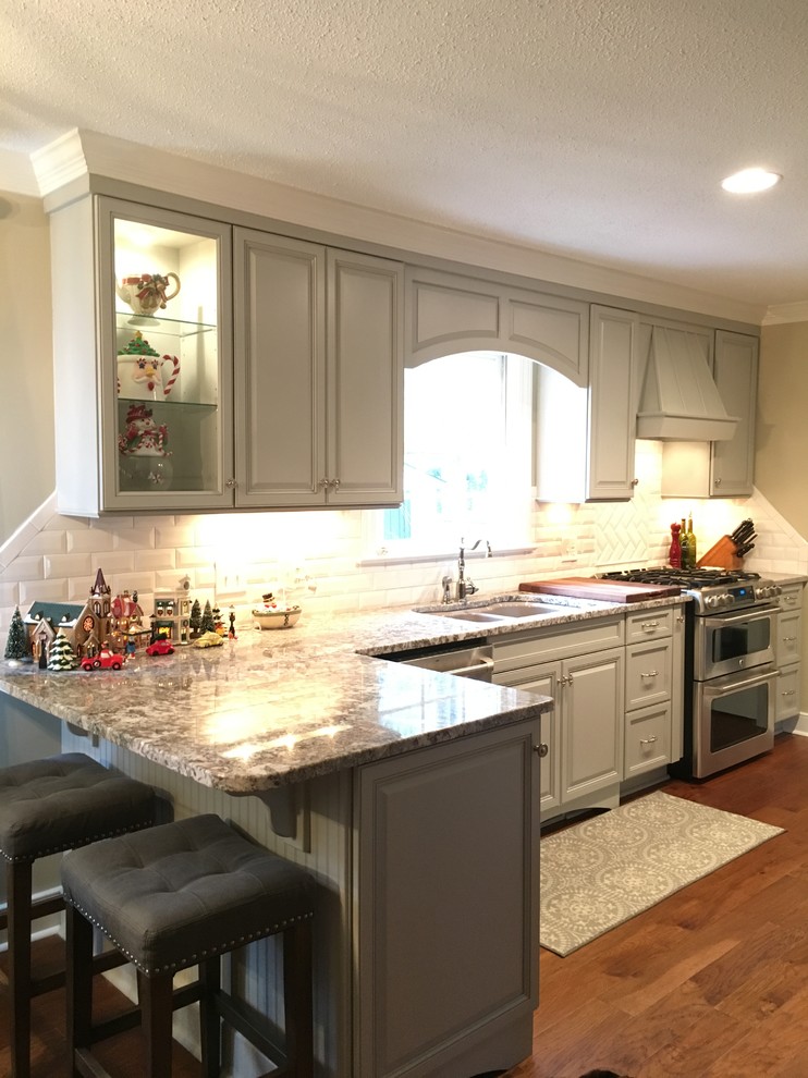 Klassisk inredning av ett mellanstort kök och matrum, med en undermonterad diskho, luckor med upphöjd panel, grå skåp, granitbänkskiva, gult stänkskydd, stänkskydd i tunnelbanekakel, rostfria vitvaror, mellanmörkt trägolv och en halv köksö