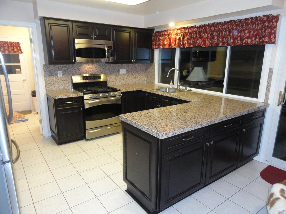 This is an example of a medium sized contemporary u-shaped kitchen/diner in Baltimore with stainless steel appliances, ceramic flooring, a breakfast bar, a submerged sink, raised-panel cabinets and black cabinets.