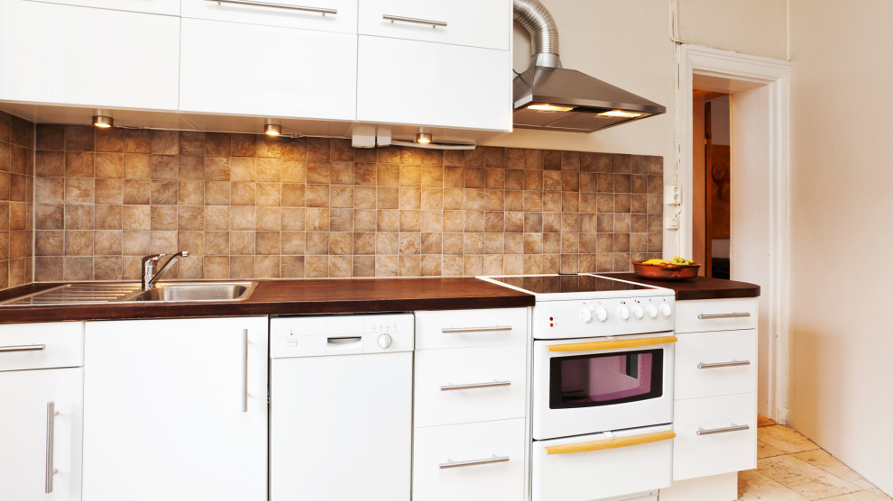 Bild på ett stort funkis brun linjärt brunt kök, med en integrerad diskho, släta luckor, vita skåp, laminatbänkskiva, beige stänkskydd, stänkskydd i skiffer, rostfria vitvaror, linoleumgolv, en köksö och beiget golv