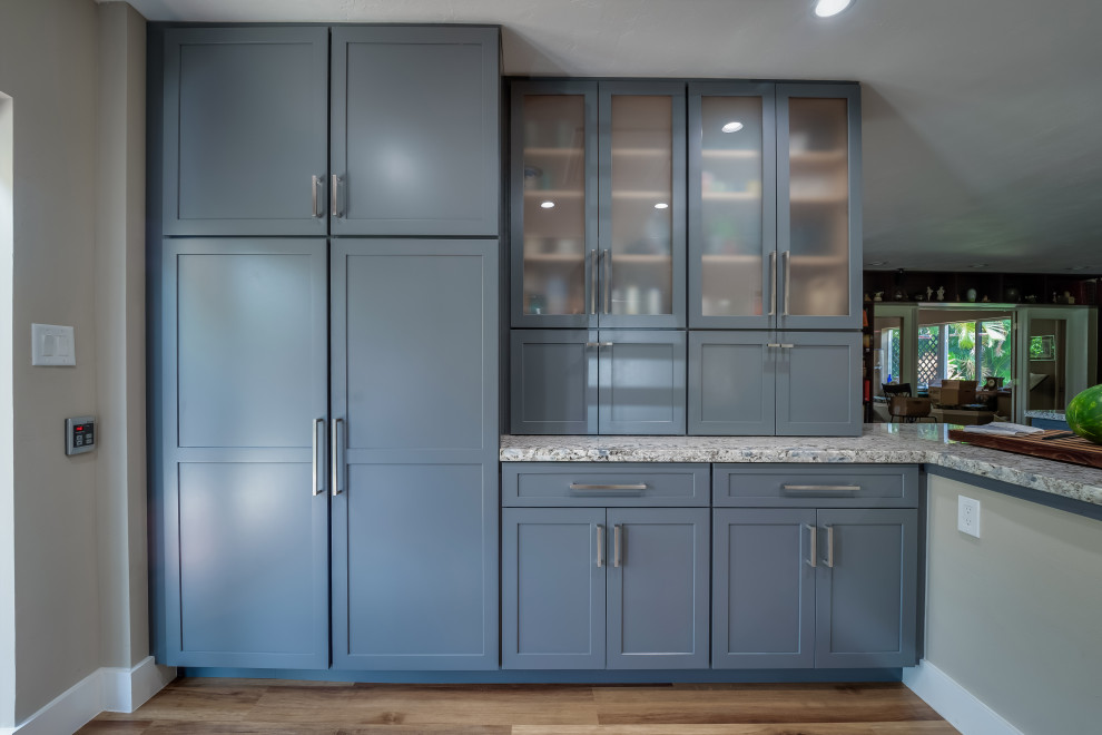 This is an example of a large rural grey and cream l-shaped kitchen pantry in Miami with a belfast sink, shaker cabinets, blue cabinets, granite worktops, beige splashback, tonge and groove splashback, stainless steel appliances, vinyl flooring, a breakfast bar, brown floors and multicoloured worktops.