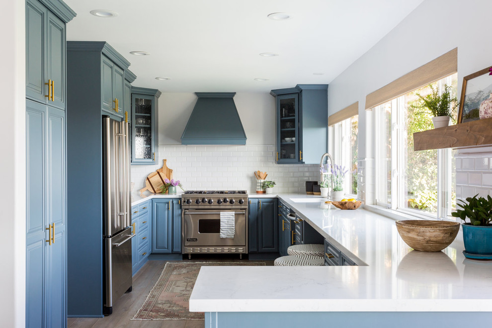 Kitchen - coastal u-shaped kitchen idea in Los Angeles with a single-bowl sink, raised-panel cabinets, blue cabinets, white backsplash, subway tile backsplash, stainless steel appliances, a peninsula and white countertops
