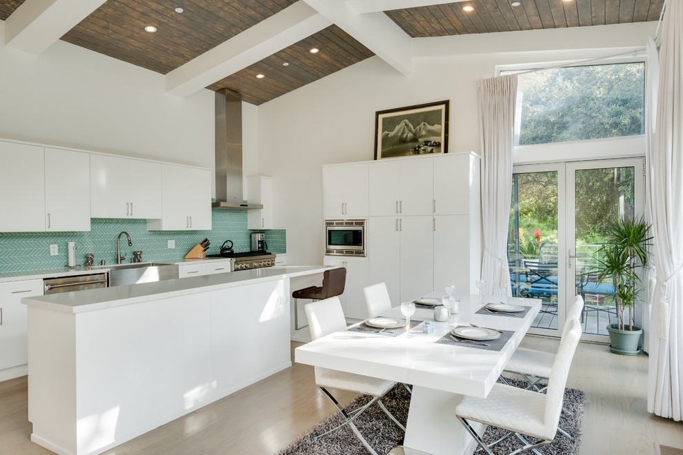 Eat-in kitchen - mid-sized contemporary single-wall light wood floor and white floor eat-in kitchen idea in Los Angeles with a farmhouse sink, flat-panel cabinets, white cabinets, quartz countertops, green backsplash, glass tile backsplash, stainless steel appliances and an island