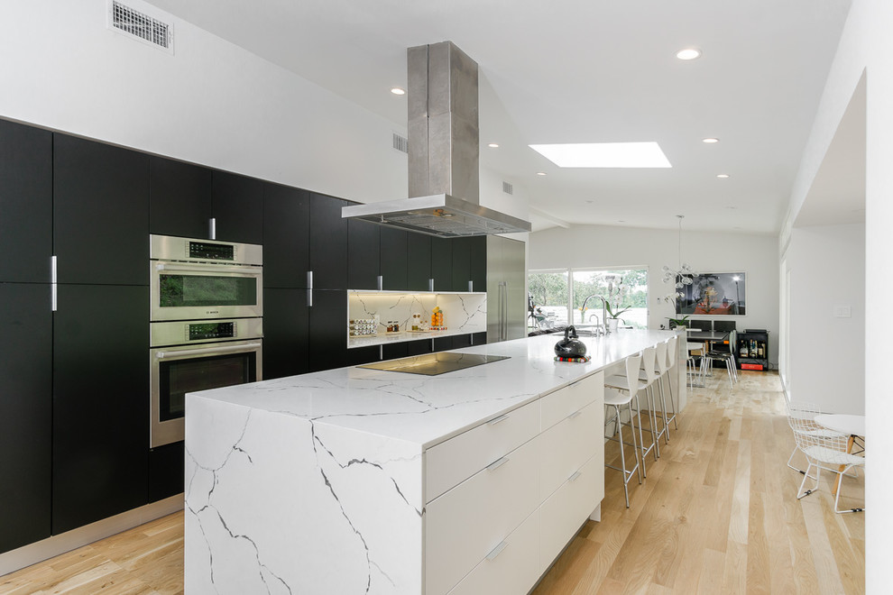 Inspiration for a contemporary galley kitchen in Los Angeles with flat-panel cabinets, stainless steel appliances, light hardwood flooring, an island, beige floors and white worktops.