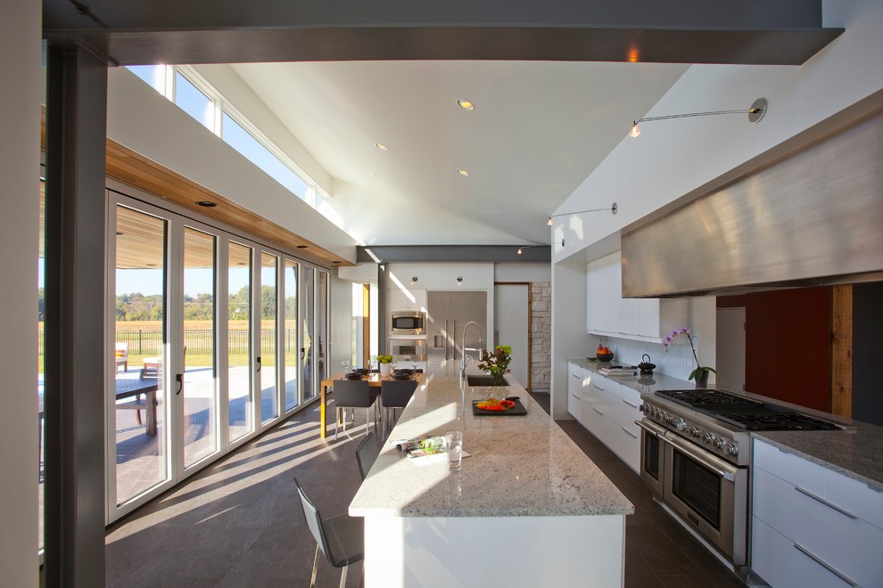 Foto på ett funkis linjärt kök med öppen planlösning, med en undermonterad diskho, släta luckor, vita skåp, granitbänkskiva, vitt stänkskydd, glaspanel som stänkskydd och rostfria vitvaror