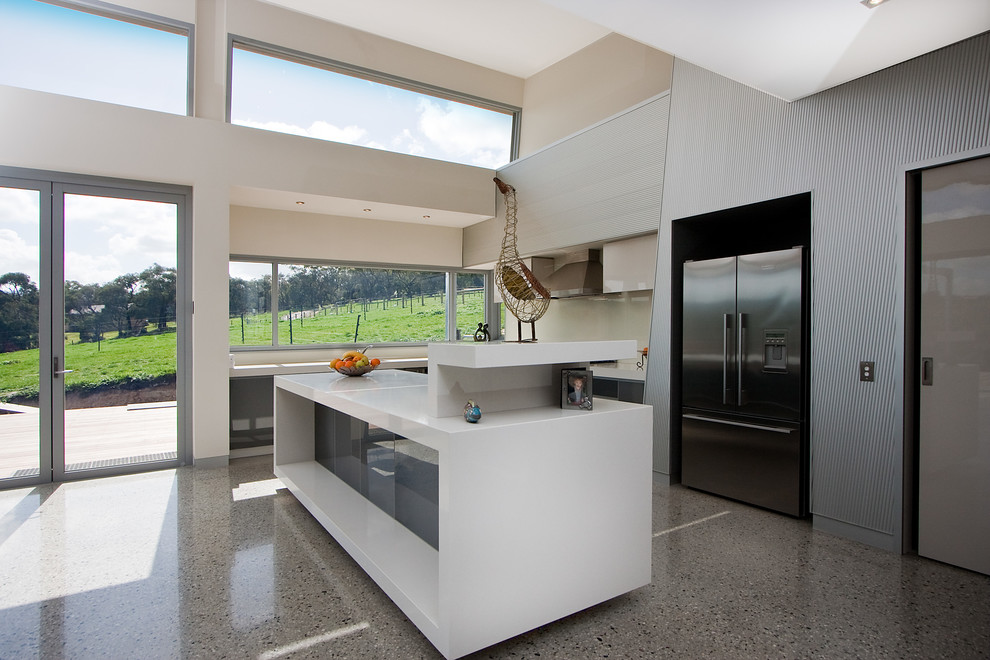 Идея дизайна: угловая кухня-гостиная в стиле модернизм с врезной мойкой, стеклянными фасадами, столешницей из кварцевого агломерата, белым фартуком, фартуком из стекла, техникой из нержавеющей стали, бетонным полом и островом