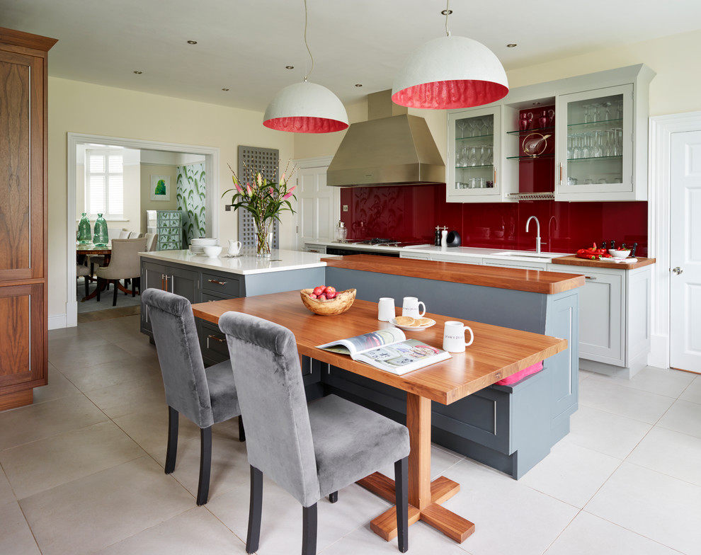 Пример оригинального дизайна: большая кухня в стиле неоклассика (современная классика) с обеденным столом, серыми фасадами, столешницей из кварцита, красным фартуком, фартуком из стекла, техникой под мебельный фасад и островом