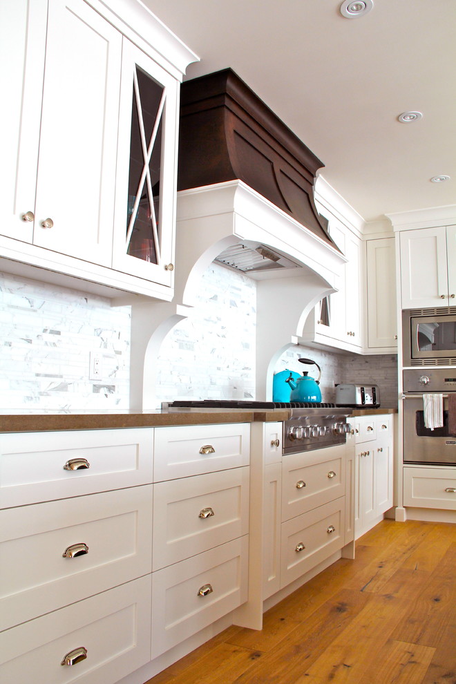 Imagen de cocina costera grande con fregadero bajoencimera, armarios estilo shaker, electrodomésticos de acero inoxidable y suelo de madera clara