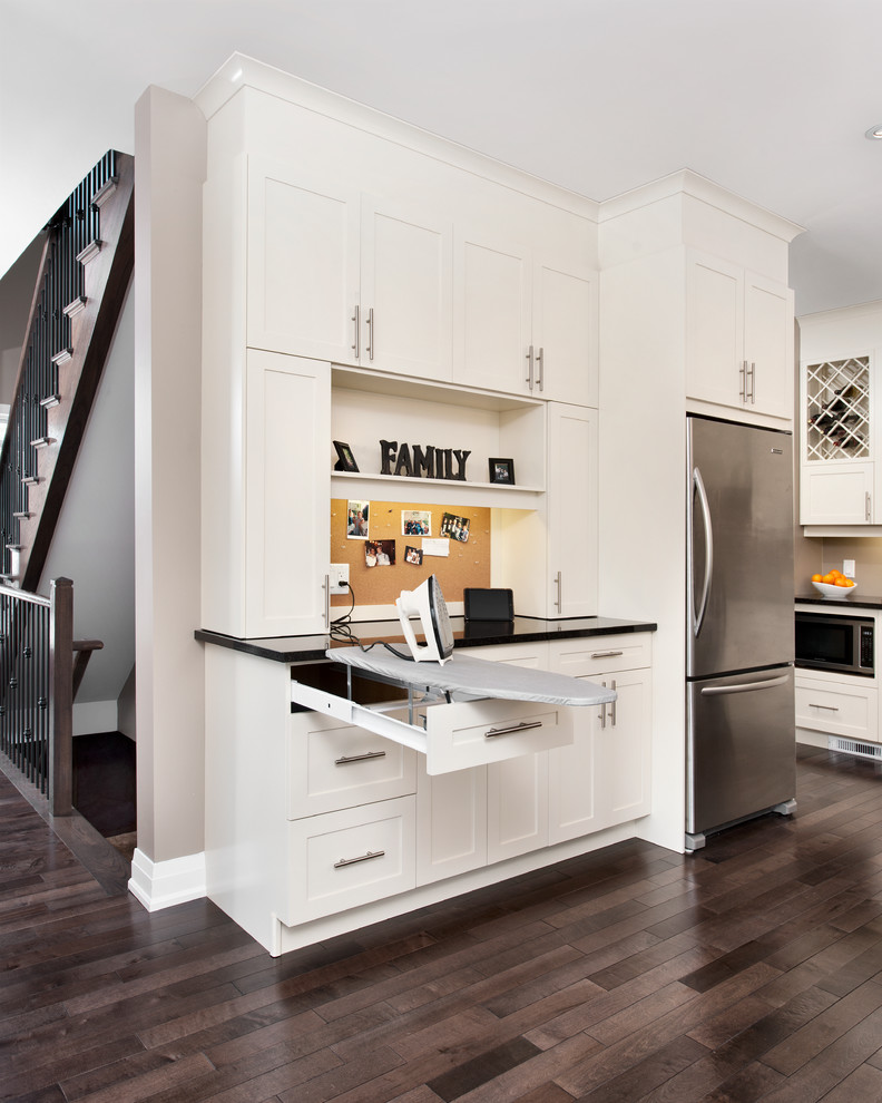 Modelo de cocina tradicional grande con armarios estilo shaker, puertas de armario blancas, encimera de acrílico, electrodomésticos de acero inoxidable y suelo de madera oscura