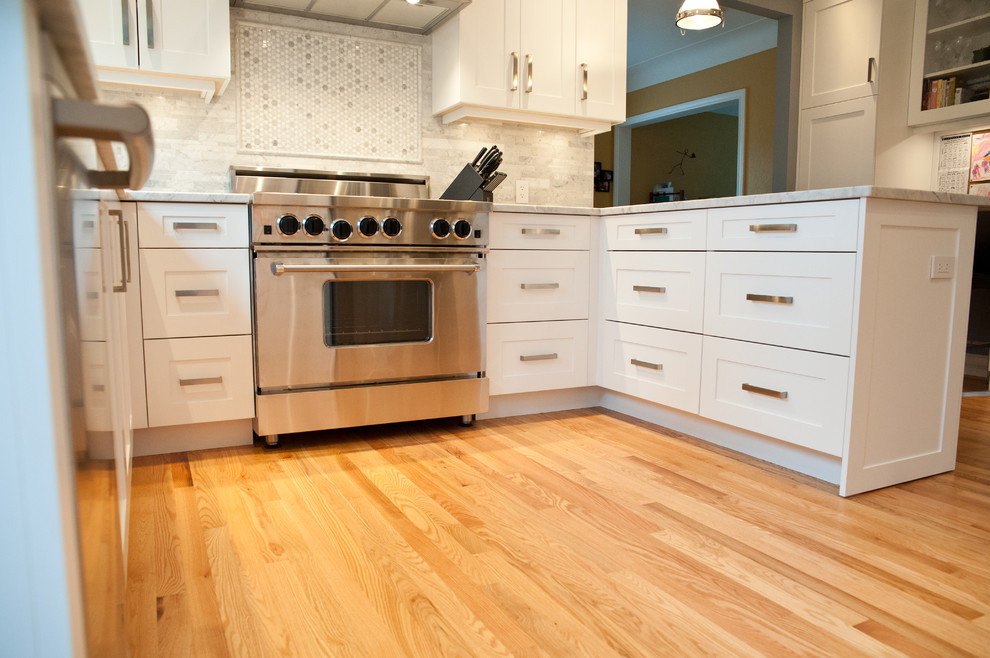 This is an example of a medium sized classic u-shaped kitchen pantry in Vancouver with a submerged sink, shaker cabinets, white cabinets, marble worktops, grey splashback, stainless steel appliances, light hardwood flooring and a breakfast bar.