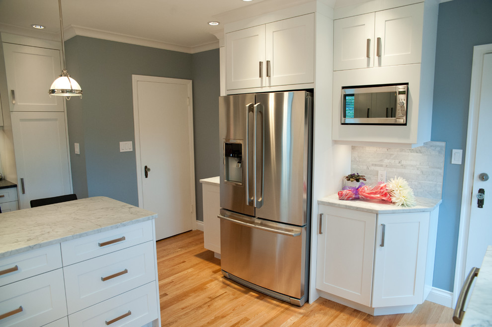 Klassisk inredning av ett mellanstort kök, med en undermonterad diskho, skåp i shakerstil, vita skåp, marmorbänkskiva, grått stänkskydd, rostfria vitvaror, ljust trägolv och en halv köksö