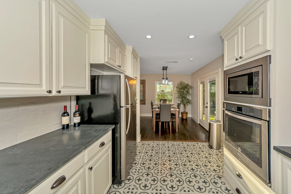 Example of a small farmhouse galley ceramic tile and multicolored floor eat-in kitchen design in Dallas with an undermount sink, raised-panel cabinets, white cabinets, granite countertops, gray backsplash, ceramic backsplash, stainless steel appliances and black countertops