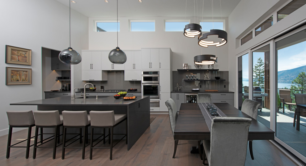 Offene, Zweizeilige Moderne Küche mit Unterbauwaschbecken, flächenbündigen Schrankfronten, weißen Schränken, Küchenrückwand in Grau, Küchengeräten aus Edelstahl, dunklem Holzboden, Kücheninsel, braunem Boden und grauer Arbeitsplatte in Vancouver