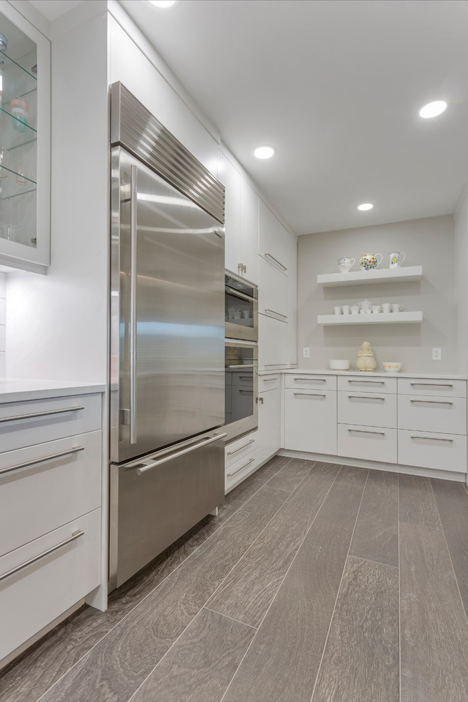 Large trendy u-shaped medium tone wood floor and gray floor enclosed kitchen photo in Tampa with an undermount sink, flat-panel cabinets, white cabinets, quartz countertops, white backsplash, ceramic backsplash, stainless steel appliances and white countertops