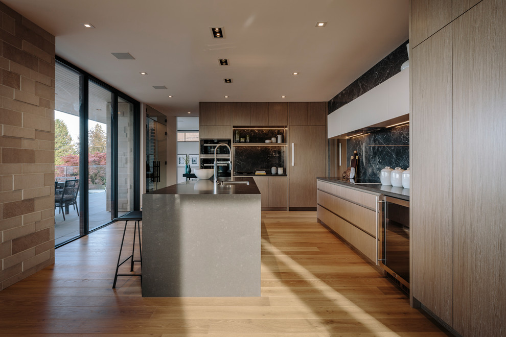 Large contemporary galley kitchen/diner in Vancouver with a submerged sink, flat-panel cabinets, medium wood cabinets, engineered stone countertops, grey splashback, porcelain splashback, stainless steel appliances, medium hardwood flooring, an island and grey worktops.