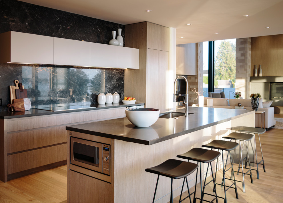 Large contemporary galley kitchen/diner in Vancouver with a submerged sink, flat-panel cabinets, medium wood cabinets, engineered stone countertops, grey splashback, porcelain splashback, stainless steel appliances, medium hardwood flooring, an island and grey worktops.
