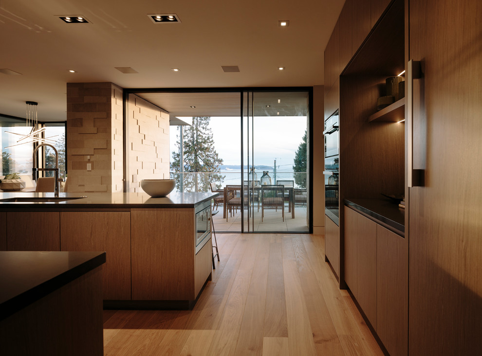 Design ideas for a large contemporary galley kitchen/diner in Vancouver with a submerged sink, flat-panel cabinets, medium wood cabinets, engineered stone countertops, grey splashback, porcelain splashback, stainless steel appliances, medium hardwood flooring, an island and grey worktops.