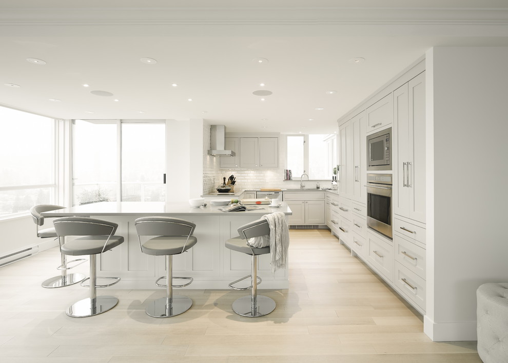 Exempel på ett mellanstort klassiskt u-kök, med en undermonterad diskho, skåp i shakerstil, grå skåp, bänkskiva i kvarts, vitt stänkskydd, stänkskydd i keramik, rostfria vitvaror, ljust trägolv och en köksö