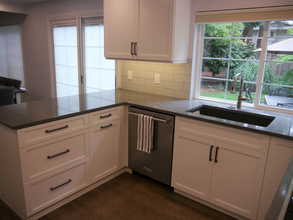Inredning av ett klassiskt stort grå grått kök och matrum, med en undermonterad diskho, luckor med infälld panel, vita skåp, bänkskiva i kvarts, vitt stänkskydd, stänkskydd i keramik, rostfria vitvaror, mellanmörkt trägolv, en halv köksö och brunt golv