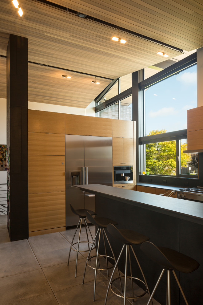 Example of a large mid-century modern u-shaped concrete floor open concept kitchen design in Seattle with an integrated sink, flat-panel cabinets, light wood cabinets, solid surface countertops, black backsplash, stainless steel appliances and an island