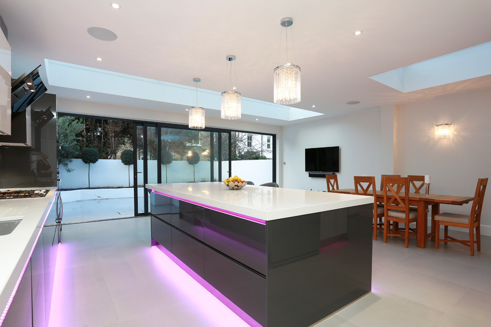 This is an example of an expansive contemporary kitchen/diner in London with a submerged sink, grey cabinets, glass sheet splashback, stainless steel appliances, ceramic flooring and an island.