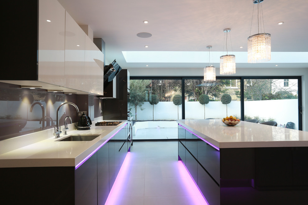 Photo of an expansive contemporary kitchen/diner in London with a submerged sink, grey cabinets, glass sheet splashback, stainless steel appliances, ceramic flooring and an island.