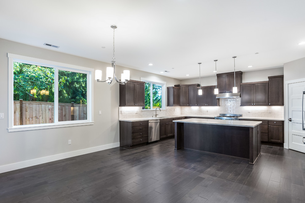 Example of a mid-sized classic u-shaped dark wood floor and brown floor open concept kitchen design in Seattle with an undermount sink, recessed-panel cabinets, dark wood cabinets, quartz countertops, white backsplash, porcelain backsplash, stainless steel appliances and an island