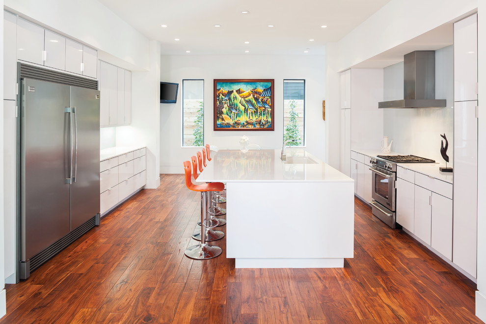This is an example of a large contemporary kitchen in Seattle with flat-panel cabinets, a submerged sink, white cabinets, engineered stone countertops, white splashback, glass sheet splashback, stainless steel appliances, medium hardwood flooring and an island.