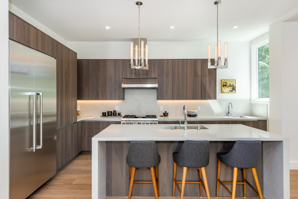 Inspiration for a mid-sized contemporary l-shaped medium tone wood floor and brown floor kitchen remodel in San Francisco with an undermount sink, flat-panel cabinets, quartz countertops, white backsplash, quartz backsplash, stainless steel appliances, an island, white countertops and dark wood cabinets