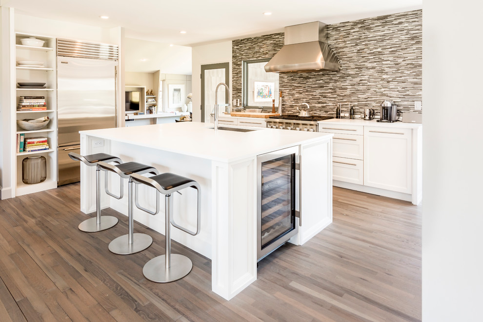 Inspiration for a large contemporary l-shaped kitchen/diner in New York with a submerged sink, shaker cabinets, white cabinets, matchstick tiled splashback, stainless steel appliances, an island, quartz worktops, multi-coloured splashback, light hardwood flooring, brown floors and white worktops.