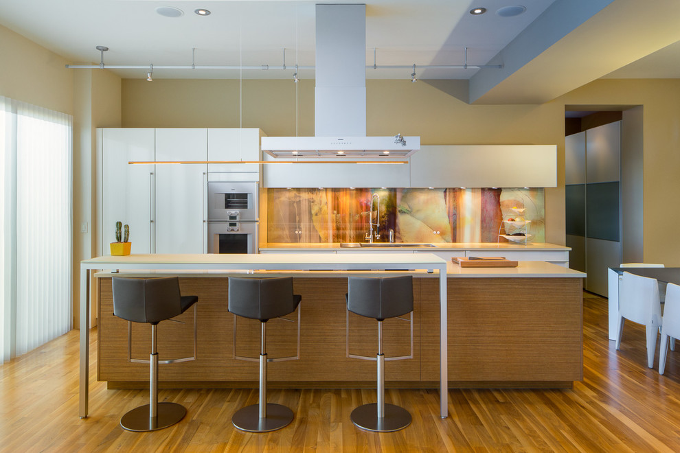 Moderne Küche mit flächenbündigen Schrankfronten, weißen Schränken, bunter Rückwand, Küchengeräten aus Edelstahl, braunem Holzboden und Kücheninsel in Denver
