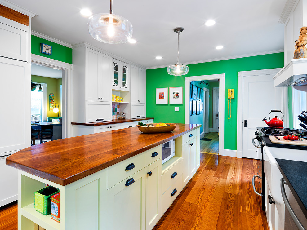 Example of a mid-sized eclectic galley medium tone wood floor and brown floor enclosed kitchen design in Boston with a farmhouse sink, shaker cabinets, wood countertops, multicolored backsplash, ceramic backsplash, paneled appliances, an island and white cabinets
