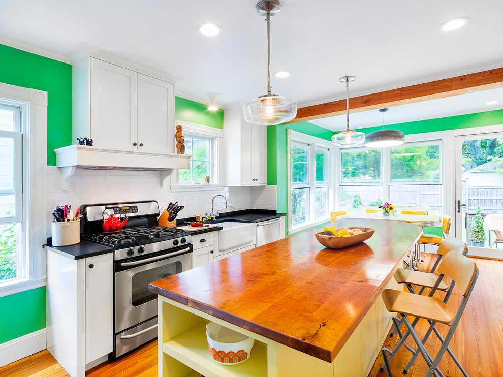 Eat-in kitchen - mid-sized eclectic galley light wood floor eat-in kitchen idea in Boston with a farmhouse sink, shaker cabinets, yellow cabinets, wood countertops, multicolored backsplash, ceramic backsplash, paneled appliances and an island