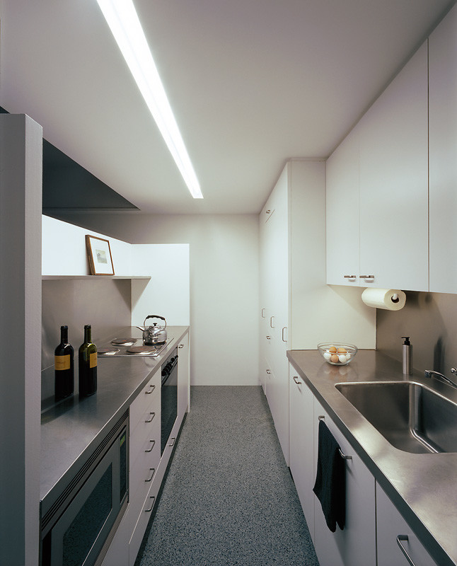 Moderne Küche mit integriertem Waschbecken, flächenbündigen Schrankfronten, Edelstahl-Arbeitsplatte, Küchengeräten aus Edelstahl, Terrazzo-Boden und grauem Boden