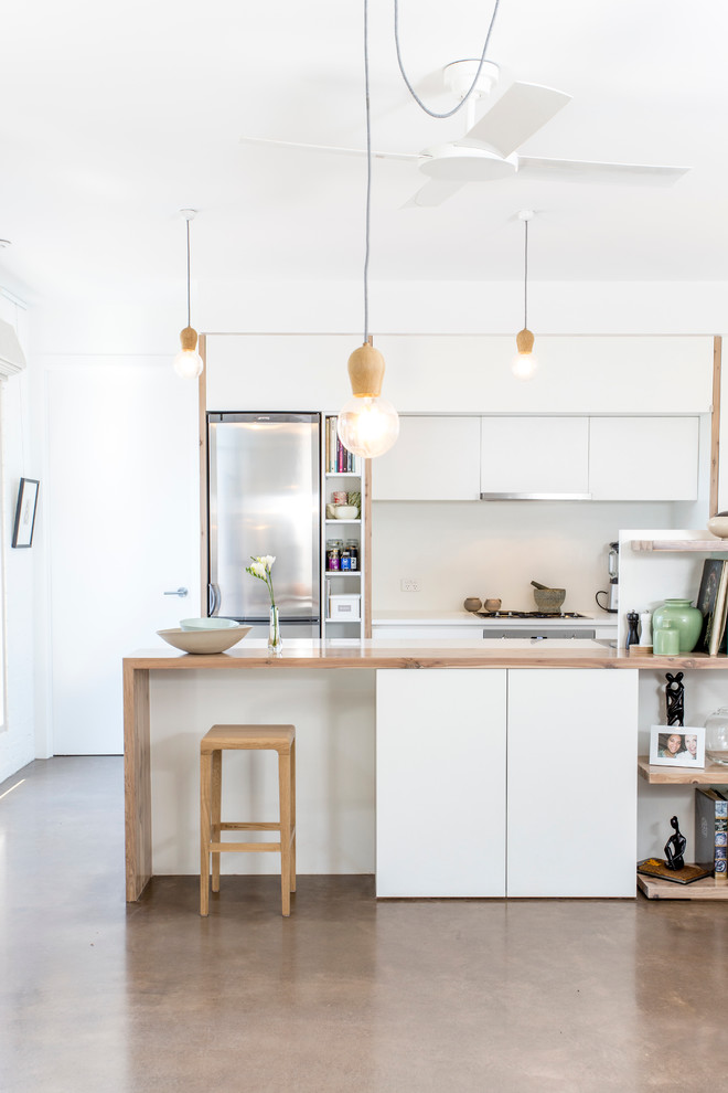 Bild på ett funkis kök, med släta luckor, vita skåp, rostfria vitvaror, betonggolv och en halv köksö