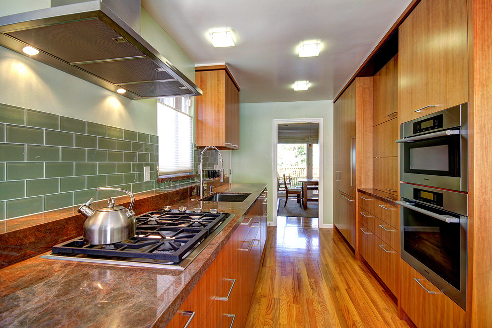 サンフランシスコにあるラグジュアリーな小さなコンテンポラリースタイルのおしゃれなキッチン (シングルシンク、フラットパネル扉のキャビネット、中間色木目調キャビネット、緑のキッチンパネル、セラミックタイルのキッチンパネル、シルバーの調理設備、無垢フローリング、人工大理石カウンター、アイランドなし、オレンジの床) の写真