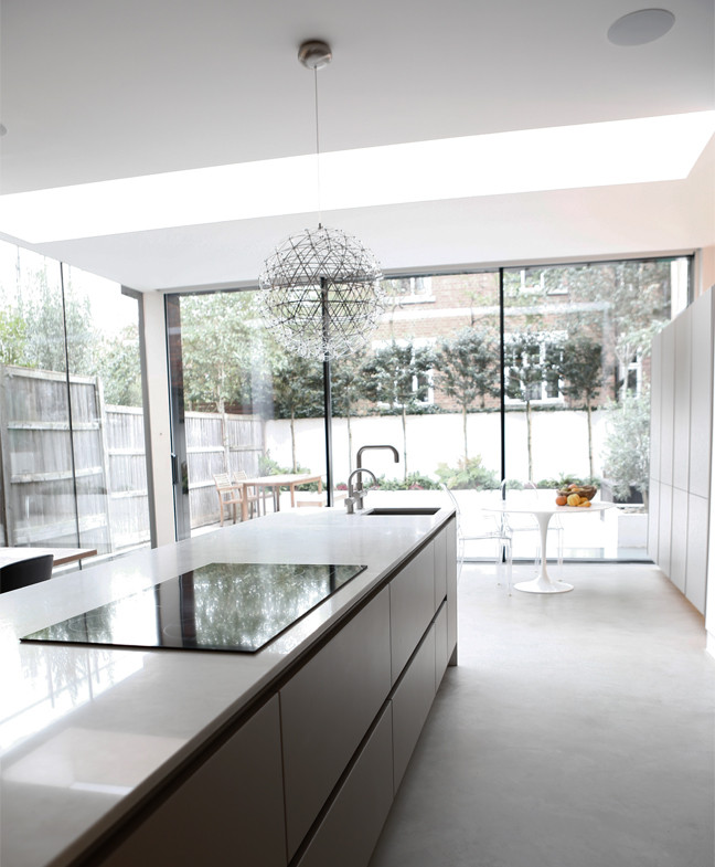 Large contemporary kitchen/diner in London with a built-in sink, flat-panel cabinets, grey cabinets, white splashback, black appliances, concrete flooring, an island, grey floors and white worktops.