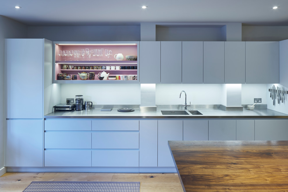 Einzeilige Moderne Küche mit flächenbündigen Schrankfronten, Edelstahl-Arbeitsplatte, hellem Holzboden, Kücheninsel, Doppelwaschbecken und weißen Schränken in London