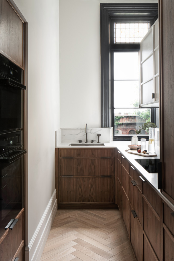 Design ideas for a traditional u-shaped kitchen in London with a submerged sink, flat-panel cabinets, dark wood cabinets, black appliances, medium hardwood flooring, no island, brown floors and white worktops.