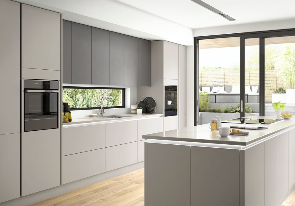 Modelo de cocina moderna grande abierta con fregadero integrado, armarios con paneles lisos, puertas de armario grises, electrodomésticos negros y una isla