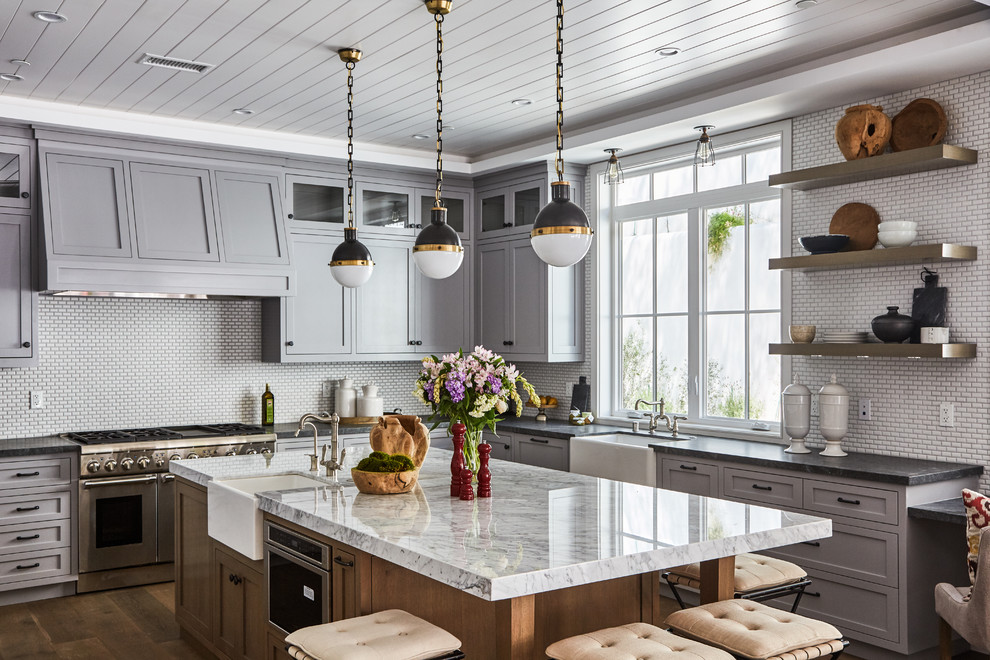 Klassische Küche in L-Form mit Landhausspüle, Schrankfronten im Shaker-Stil, grauen Schränken, Küchengeräten aus Edelstahl, braunem Holzboden und Kücheninsel in Los Angeles