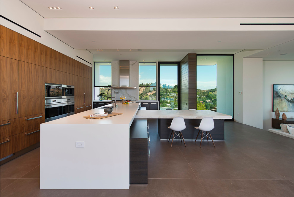 Example of a trendy l-shaped gray floor eat-in kitchen design in Los Angeles with an undermount sink, flat-panel cabinets, medium tone wood cabinets, white backsplash, window backsplash, stainless steel appliances, an island and white countertops