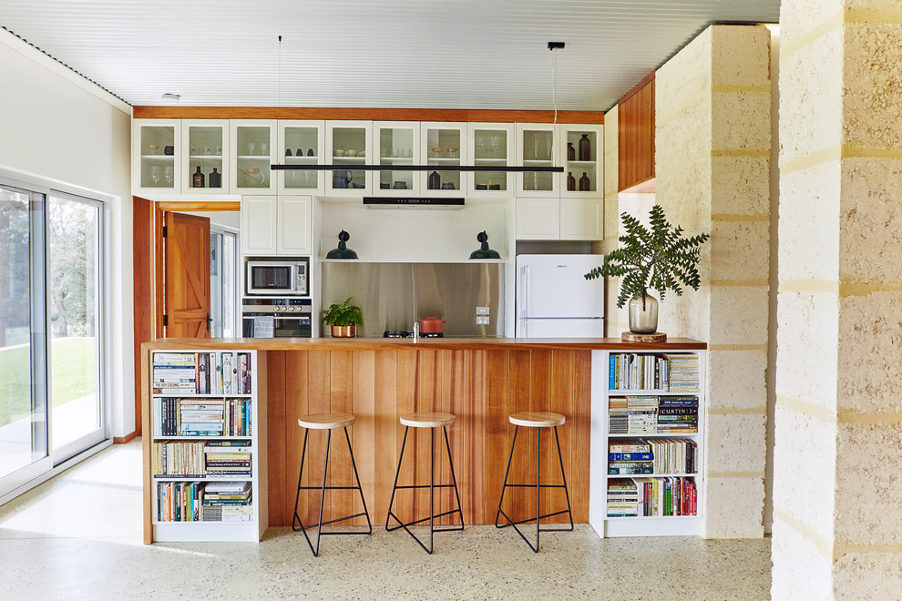 Exempel på ett mellanstort klassiskt brun brunt kök, med luckor med glaspanel, vita skåp, träbänkskiva, stänkskydd med metallisk yta, rostfria vitvaror, betonggolv, grått golv och en halv köksö
