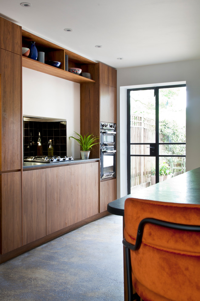 This is an example of a medium sized galley kitchen/diner in London with a double-bowl sink, flat-panel cabinets, brown cabinets, blue splashback, black appliances, concrete flooring, a breakfast bar and grey worktops.