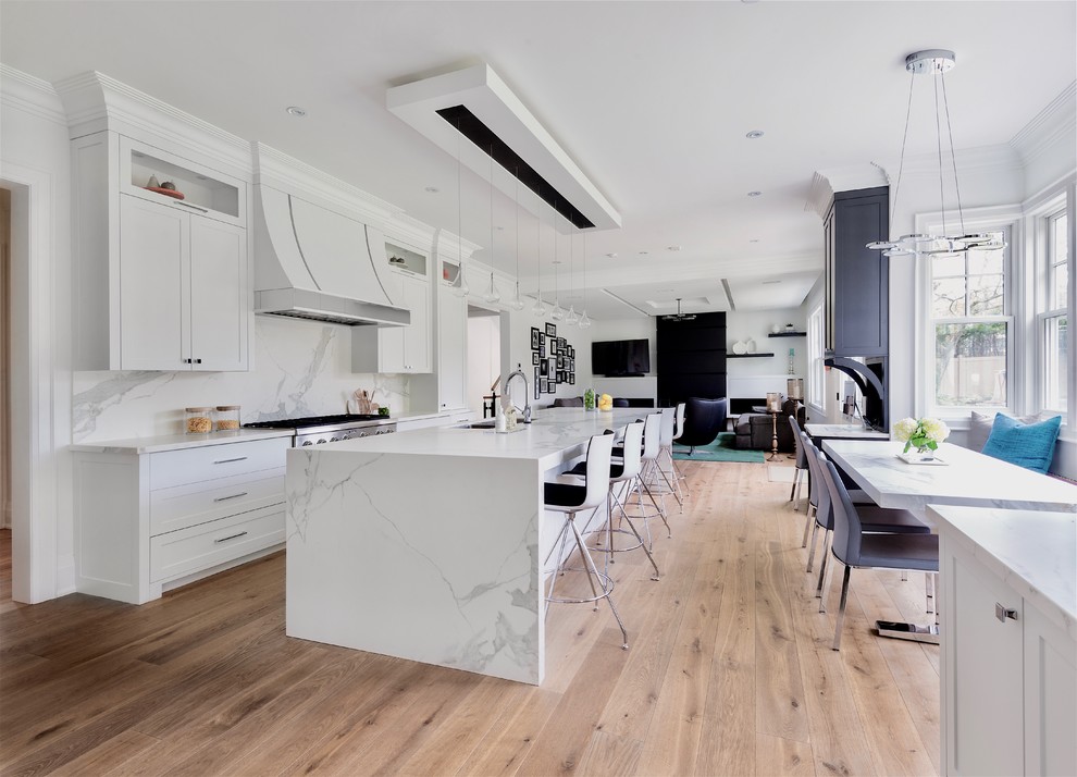This is an example of a large contemporary galley open plan kitchen in Toronto with a submerged sink, shaker cabinets, white cabinets, white splashback, stainless steel appliances, medium hardwood flooring, an island, brown floors, marble worktops and marble splashback.