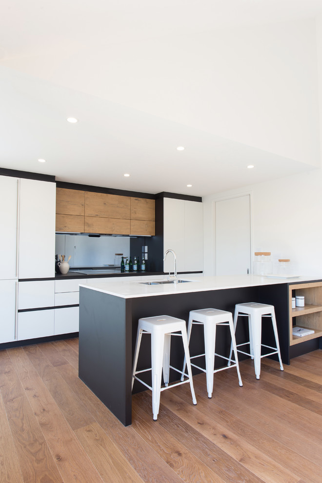 Inspiration for a modern galley open plan kitchen in Christchurch with a double-bowl sink, white cabinets, engineered stone countertops, black splashback, glass sheet splashback, stainless steel appliances, medium hardwood flooring and an island.