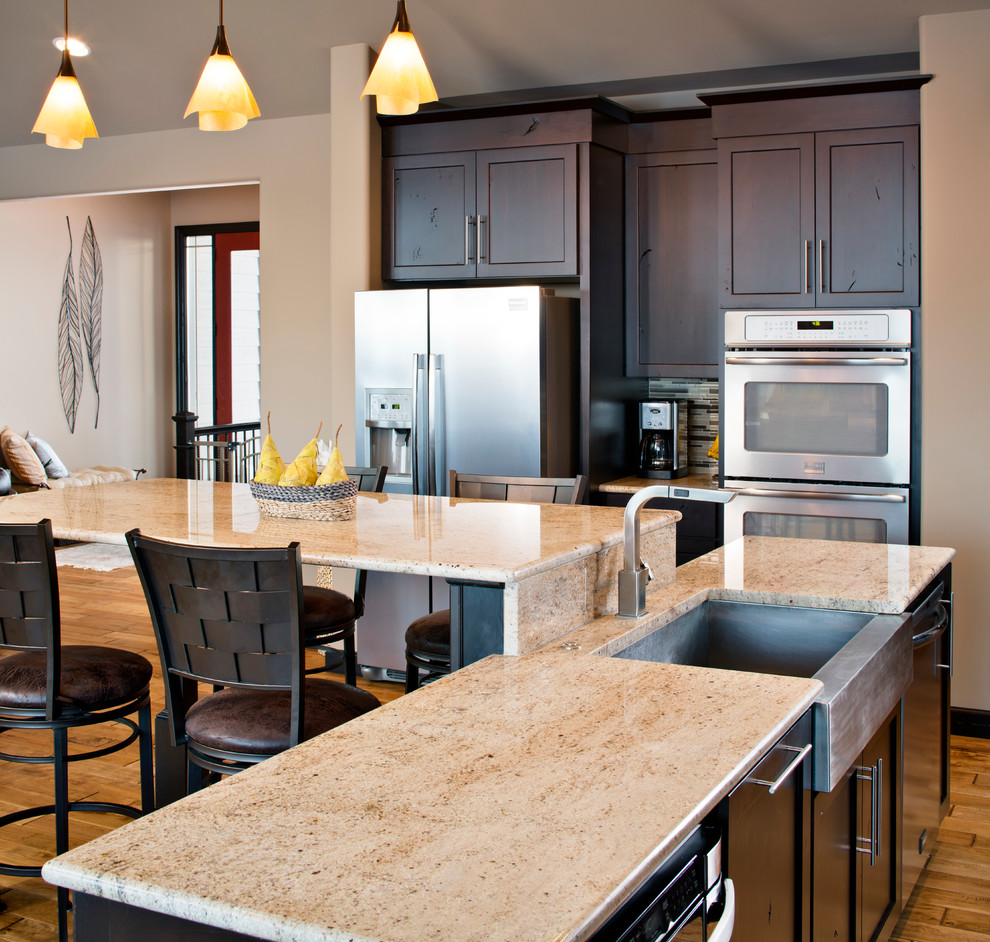 Eat-in kitchen - large modern l-shaped light wood floor eat-in kitchen idea in Omaha with dark wood cabinets, multicolored backsplash, stainless steel appliances, a farmhouse sink, granite countertops, an island, recessed-panel cabinets and mosaic tile backsplash