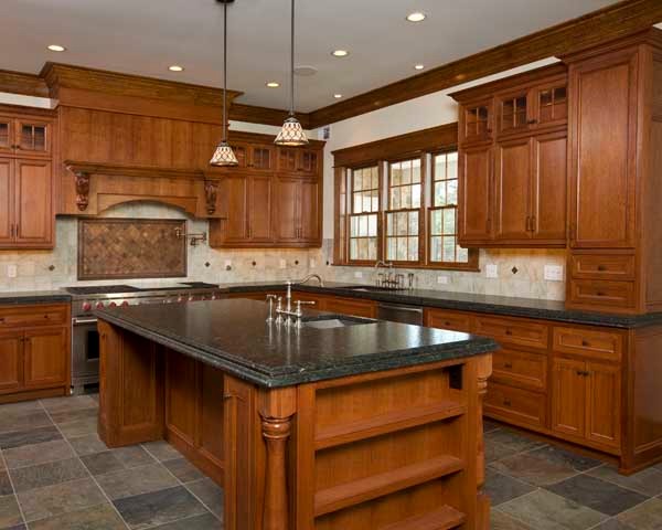 Inredning av ett klassiskt mellanstort l-kök, med en enkel diskho, luckor med infälld panel, skåp i mellenmörkt trä, granitbänkskiva, beige stänkskydd, stänkskydd i keramik, skiffergolv, en köksö och flerfärgat golv