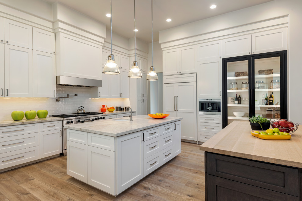 Transitional medium tone wood floor and brown floor enclosed kitchen photo in Phoenix with an undermount sink, shaker cabinets, white cabinets, wood countertops, white backsplash, subway tile backsplash, paneled appliances, two islands and brown countertops